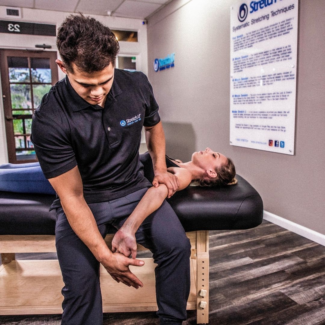 A male therapist applies targeted pressure to a female client's forearm and bicep area, demonstrating a myofascial release technique.